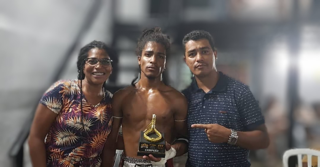 Christofer segurando o troféu de campeão de um evento da FTT, entre os pais